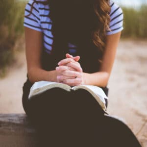 Exploring Prayers from the Old Testament lady in prayer while sitting outside with an open Bible on her lap and interlocked fingers on top of Bible