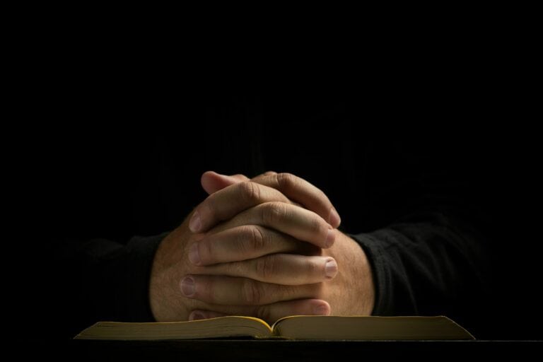 Prayer with open Bible and intertwined hands on top of it