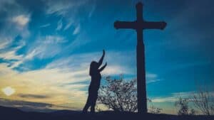 Exploring the Transformational Power of Surrender lady with arms outstretched to a cross with a blue sky in the background