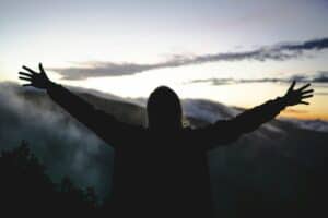 Exploring the Transformational Power of Surrender Lady with arms outstretched towards the sky and mountains covered with fog
